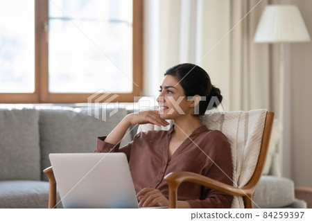 Woman relaxing on armchair with laptop staring into distance daydreaming 84259397