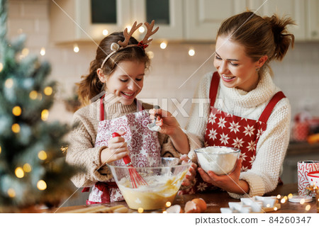 Cute little daughter girl helping mother to make dough for Christmas cookies in cozy kitchen at home 84260347