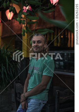 Portrait of elderly man in t-shirt, jeans on the green street. Long grey hair. Chinese lanterns. Evening. High quality photo 84261295