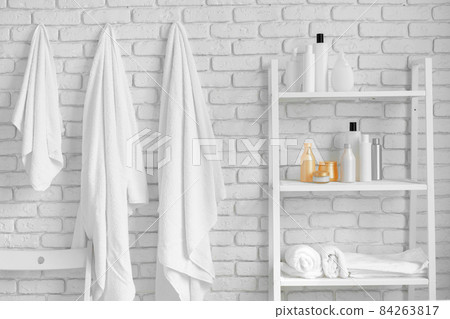 Bathroom shelving with cosmetic bottles and hanging towels against white brick wall 84263817