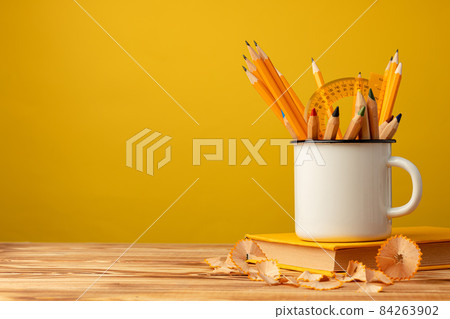 Metal cup with sharp pencils and pencil shavings on wooden desk 84263902