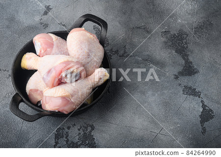 Chicken brow and drumstick with skin, in frying cast iron pan, on gray stone background, top view flat lay, with copy space for text 84264990
