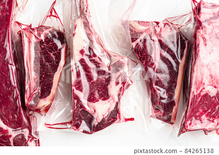 Raw marbled beef steak in vacuum packaging, tomahawk, t bone, club steak, rib eye and tenderloin cuts, on white stone background, top view flat lay 84265138