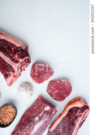 Fresh raw Prime Black Angus beef marbled and dry aged steaks, tomahawk, t bone, club steak, rib eye and tenderloin cuts, on white stone background, top view flat lay, with copy space for text Fresh raw Prime Black Angus beef marbled and dry aged steaks, tomahawk, t bone, club steak, rib eye and tenderloin cuts, on white stone background, top view flat lay, with copy space for text 84265297