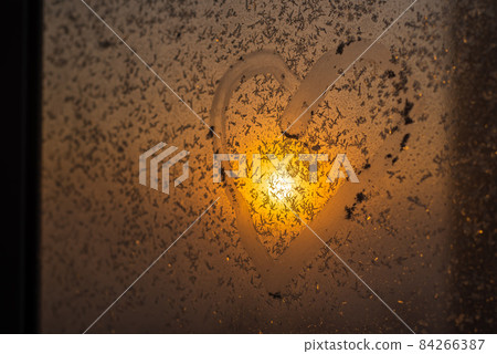 A heart drawn on a frozen winter window at sunset. 84266387