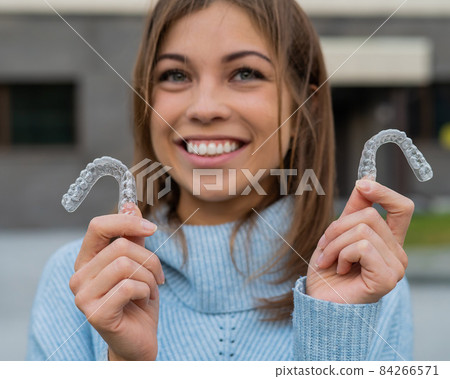 Caucasian woman with white smile holding transparent removable retainer. Bite correction device. Caucasian woman with white smile holding transparent removable retainer. Bite correction device. 84266571