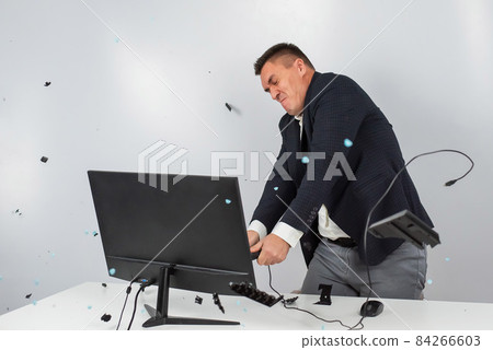 Caucasian man in a suit gets angry and smashes the keyboard on the monitor. An office worker in a rage breaks the computer. Caucasian man in a suit gets angry and smashes the keyboard on the monitor. An office worker in a rage breaks the computer. 84266603