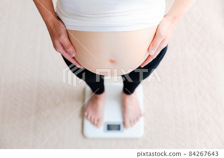 Pregnant woman riding on a weight scale Mid-pregnancy Pregnant woman riding on a weight scale Mid-pregnancy 84267643