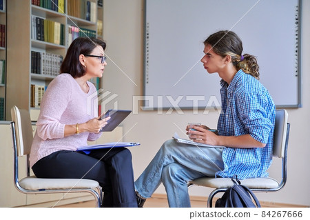 Woman school psychologist talking and helping student, teenage male Woman school psychologist talking and helping student, teenage male 84267666