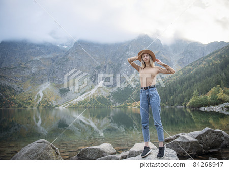 Young tourist woman in a hat with hands up on the top of the mountains Young tourist woman in a hat with hands up on the top of the mountains 84268947