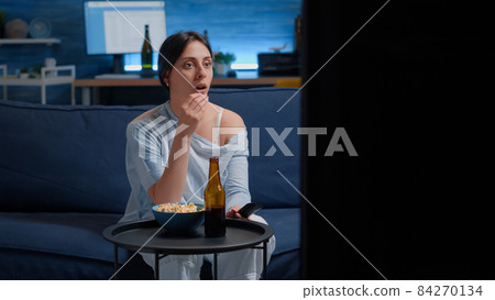 Emotional young woman eating popcorn while watching disgusting tv movie Emotional young woman eating popcorn while watching disgusting tv movie 84270134