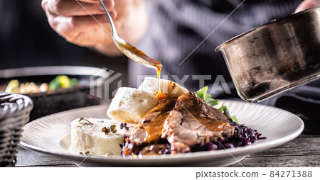Food decorating hand of a chef pours sauce over hearty food of meat, dumplings and cabbage 84271388