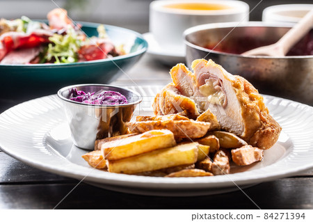 Chicken cordon bleu with ham and cheese inside served with fried potato wedges and red cabbage salad 84271394