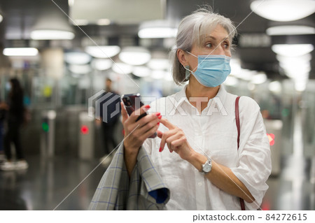 Caucasian woman in mask with smartphone in subway station 84272615