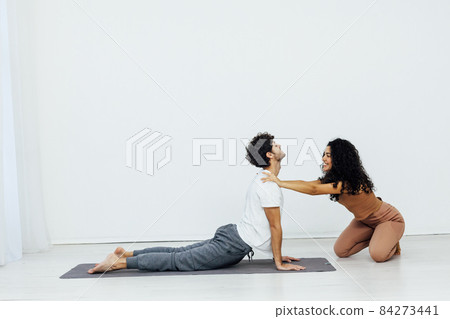 woman teaches man doing gymnastics yoga asana in a white room woman teaches man doing gymnastics yoga asana in a white room 84273441