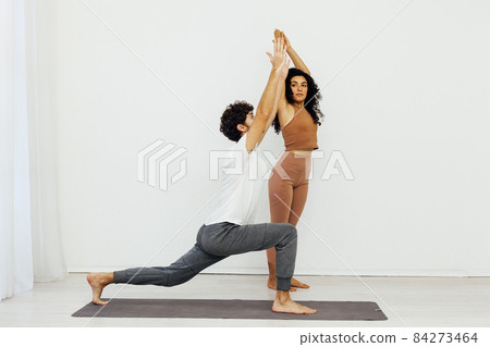 woman teaches man doing gymnastics yoga asana in a white room woman teaches man doing gymnastics yoga asana in a white room 84273464