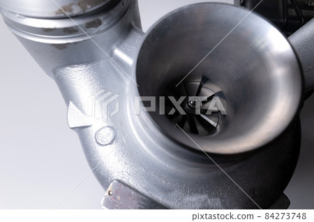 Close-up of an auto part for an internal combustion engine. Gas turbine. Turbo supercharger new on a gray background. Parts background Close-up of an auto part for an internal combustion engine. Gas turbine. Turbo supercharger new on a gray background. Parts background 84273748