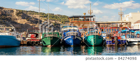 Row of many small old multicolored vintage colorful bright fishing ships moored at fisherman village marina clear water bay on bright sunny day. Sea harbor with traditional retro vessels background Row of many small old multicolored vintage colorful bright fishing ships moored at fisherman village marina clear water bay on bright sunny day. Sea harbor with traditional retro vessels background 84274098