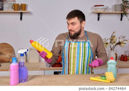 Young handsome bearded man in the kitchen, cleans up using detergents, brushes, sprays Young handsome bearded man in the kitchen, cleans up using detergents, brushes, sprays 84274464