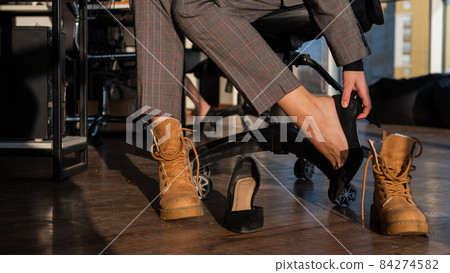 Business woman changes shoes with high heels on boots in the office. End of the working day. Tired legs 84274582