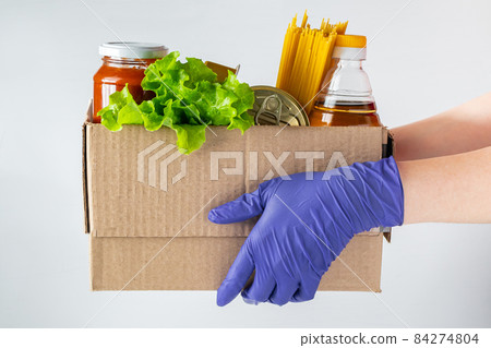 A young woman volunteer is holding a donation box with foodstuffs. Delivery of necessary food during an epidemic. A young woman volunteer is holding a donation box with foodstuffs. Delivery of necessary food during an epidemic. 84274804