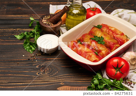 cabbage rolls stuffed with ground beef and rice with sour cream in a baking dish and ingredients 84275631