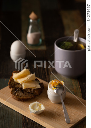 Still life breakfast. Boiled egg with salt, homemade bread with butter and cheese, tea. Front view. 84275667