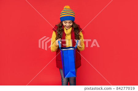 amazed child in winter clothes open shopping bag on red background, christmas shopping amazed child in winter clothes open shopping bag on red background, christmas shopping 84277019