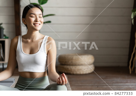 Mindfulness and meditation concept. Young asian woman doing workout at home, yoga meditation in living room on floor mat, getting focused Mindfulness and meditation concept. Young asian woman doing workout at home, yoga meditation in living room on floor mat, getting focused 84277333