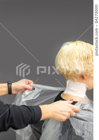 Hairstylist covers neck with cape for a female client in a beauty salon. 84278000