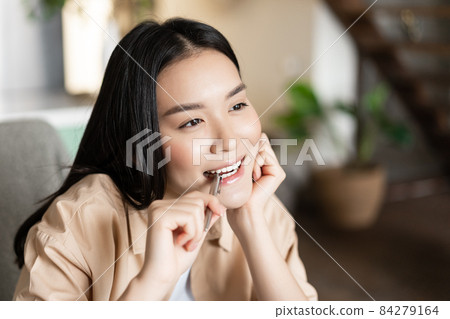 Portrait of thoughtful asian girl biting pen and smiling, thinking, searching inspiration, doing homework and getting creative 84279164