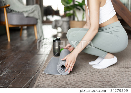 Cropped shot of woman rolling out floor mat for yoga, fitness training at home, girl prepare place for workout at home Cropped shot of woman rolling out floor mat for yoga, fitness training at home, girl prepare place for workout at home 84279299