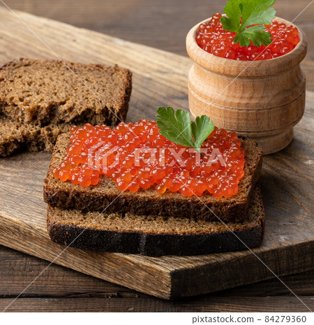 red salmon caviar lies on a piece of rye bread. Brown wooden table red salmon caviar lies on a piece of rye bread. Brown wooden table 84279360