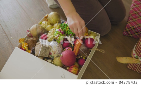 A man packing Christmas decorations in a cardboard box. Transfer of Packed Trinkets and Rolled Garlands for storage for the next year. 84279432
