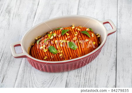 Baked hasselback pumpkin glazed with caramel in baking pan 84279835