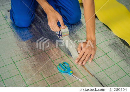 Master installs the overlapping thermal insulation in the room. Floor heating installation. Male hand holds reinforced tape. Repair in the apartment, floor insulation 84280304