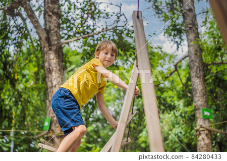 Little boy in a rope park. Active physical recreation of the child in the fresh air in the park. Training for children Little boy in a rope park. Active physical recreation of the child in the fresh air in the park. Training for children 84280433
