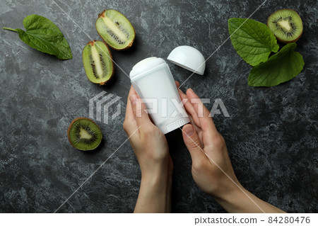 Female hands hold deodorant on black smokey background with kiwi 84280476