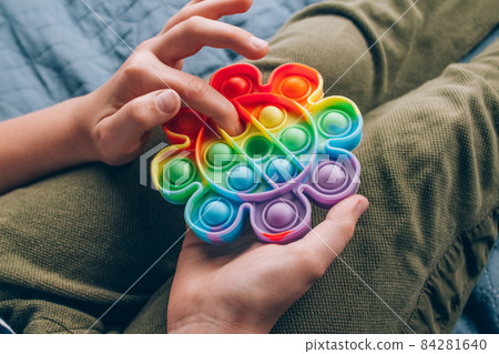 Top view on of boy's hands using rainbow pop it fidget toy. Push bubble fidget sensory toy - washable and reusable silicone stress relief toy. Antistress toy for child with special needs Top view on of boy's hands using rainbow pop it fidget toy. Push bubble fidget sensory toy - washable and reusable silicone stress relief toy. Antistress toy for child with special needs 84281640