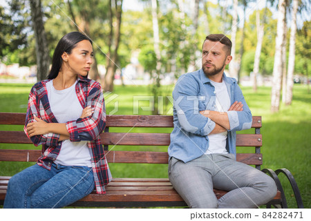 Couple is Breaking Up. Disappointed sight. Guy and girl on a bench in quarrel on a park. Relationship crisis and family break. Female resentment. 84282471