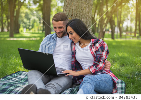 Love couple spends time in the park with a laptop. Happy couple and joint activities. Young people watching video on laptop. Love couple spends time in the park with a laptop. Happy couple and joint activities. Young people watching video on laptop. 84283433