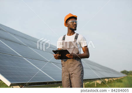 Male African technician standing with clipboard on solar station looking away 84284005