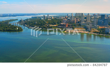Beautiful urban environment on a summer day.  Aerial view of the summer landscape with a view of the river and the city on the shore. 84284787