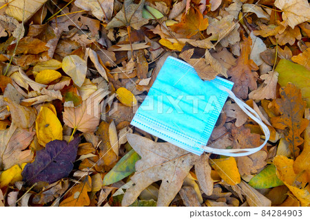A medical mask lies in the fallen leaves in the park. The beginning of a new wave of the coronavirus epidemic. The spread of COVID-19. 84284903