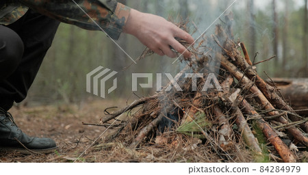 Low angle shot of a man is trying make a fire in the forest. Close-up of a man's hand lighting a campfire. Lighting a fire in the forest by a person. Low angle of a burning fire made of brushwood. Low angle shot of a man is trying make a fire in the forest. Close-up of a man's hand lighting a campfire. Lighting a fire in the forest by a person. Low angle of a burning fire made of brushwood. 84284979