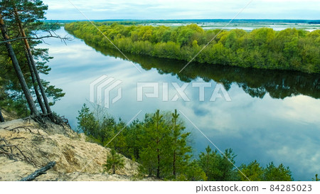 Sandy high shore, River with a view of the meadow flooded during the flood, afternoon.  Beautiful Wildlife: river, forest, meadow, roots, sky . 84285023