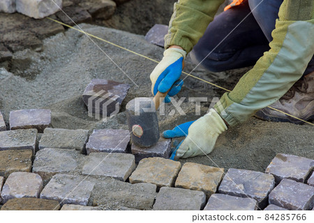 Worker using rubber hammer to laying pavement stones on sidewalk near road in city 84285766