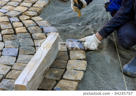 Laying granite cubes stone pavement on the a city street with construction worker 84285787