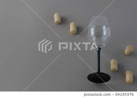 On a gray background, one empty glass wine goblet with scattered corks. The photo is horizontal. 84285976
