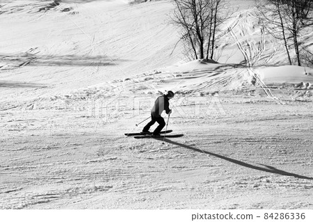 Skier downhill on snowy ski slope at winter. Black and white. High contrast. Skier downhill on snowy ski slope at winter. Black and white. High contrast. 84286336